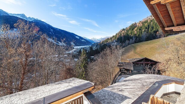 A mountain view from a wooden cabin with a snow-covered roof and a wooden deck.