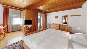 A wooden-paneled room with a bed, a TV, a dresser, and a window with curtains.