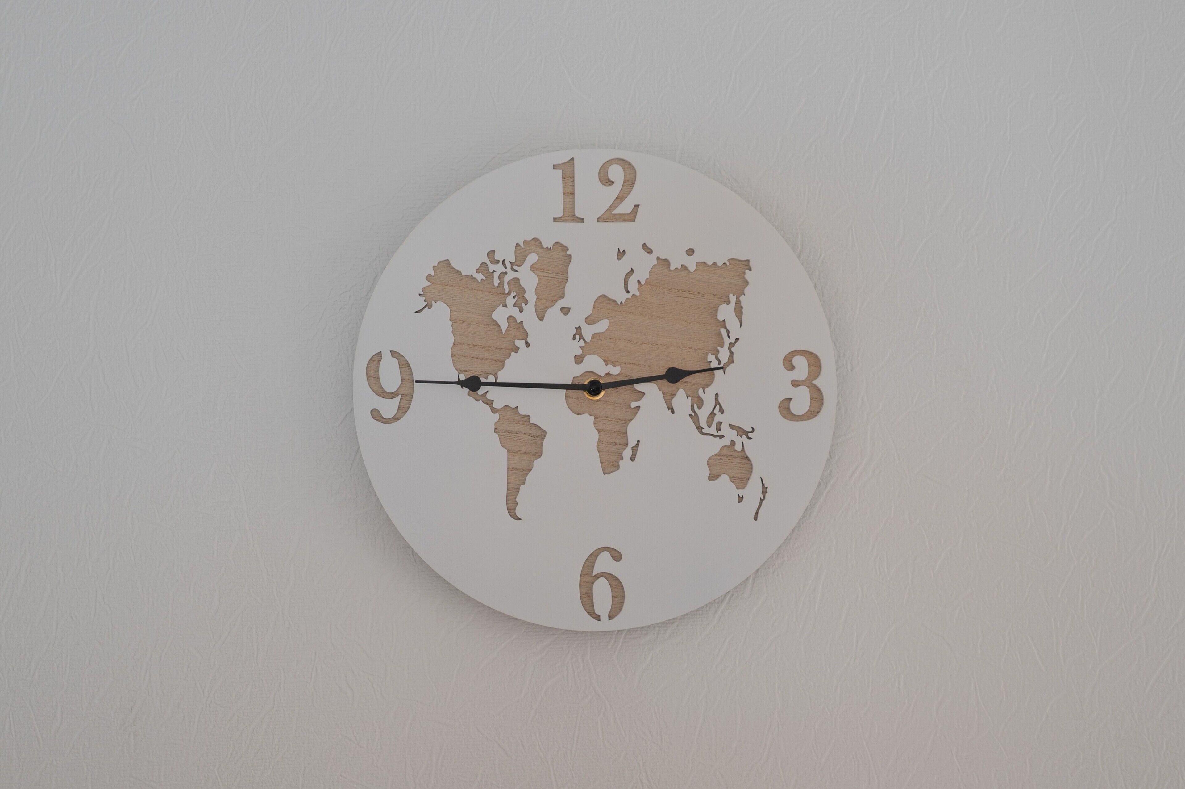 A round wall clock with a world map design and numbers 1-12.