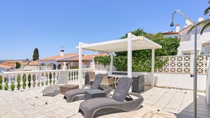 A rooftop terrace with lounge chairs, a pergola, and a view of buildings.