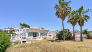 A white villa with a tiled roof, surrounded by palm trees and a well-maintained lawn.