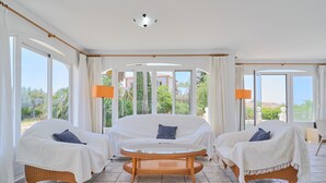 A room with a bed, two chairs, a round table, and large windows.