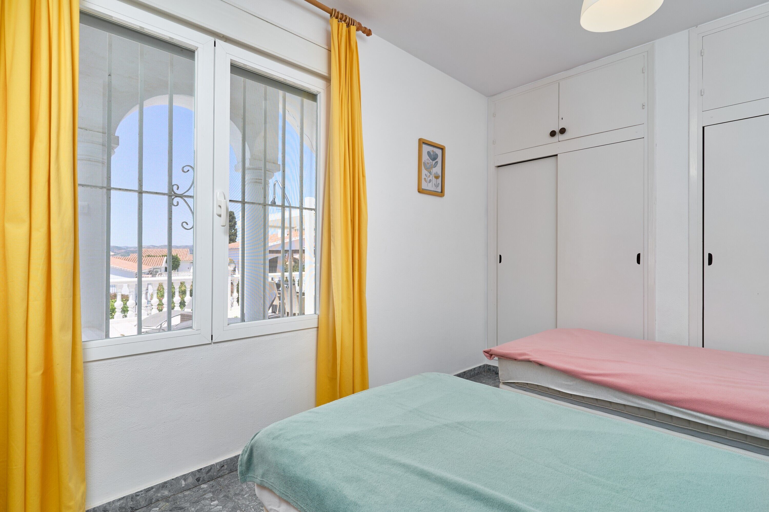 Een slaapkamer met een bed, een raam met gordijnen, een kledingkast en een foto aan de muur.