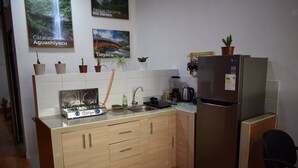 A compact kitchen with a stainless steel refrigerator, a gas stove, and a sink. There are several potted plants on the countertop, and the walls are adorned with framed pictures. - Central and Cozy Apartment (Tarapoto)