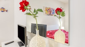 Una habitación con una cama, un televisor, un control remoto y dos jarrones con flores.