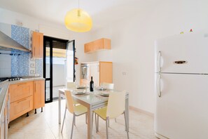 A modern kitchen with a dining table, chairs, a refrigerator, and a hanging light fixture. - Holiday Home 'Idrusa A Otranto' with Balcony, Wi-Fi and Air Conditioning (Otranto)