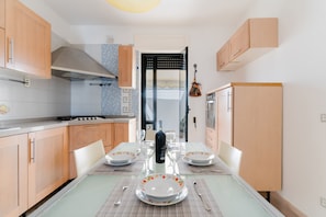 Une cuisine moderne avec des meubles en bois, une cuisinière à gaz et une table à manger dressée pour quatre personnes, avec assiettes et verres.
