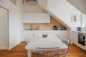 Une cuisine moderne avec des meubles blancs, une table à manger et un bar pour prendre le petit-déjeuner.