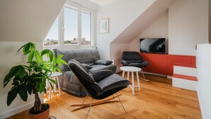 Un salon moderne avec un canapé, un fauteuil à bascule, une petite table, une plante en pot et un téléviseur.