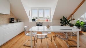 Une cuisine moderne avec une table blanche, des chaises transparentes et une vue sur la ville grâce à de grandes fenêtres.
