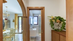 A hallway leading to a bathroom with a shower, a sink, and a mirror. There is a dining area with a table and chairs, and a plant with flowers on a cabinet. - Apartment 'Filomena 1' with Private Terrace and Air Conditioning (Torre Vado)