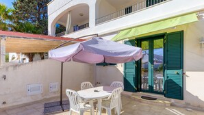 A patio with a table and chairs, a covered umbrella, and a building with green shutters. - Apartment 'Filomena 1' with Private Terrace and Air Conditioning (Torre Vado)
