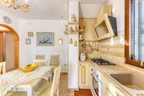 A compact kitchen with a stove, sink, and wooden cabinets. There is a dining area with a table and chairs.