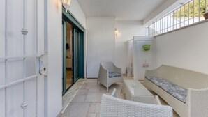 Un espace extérieur abrité comprenant un canapé en osier blanc, une chaise et une table.