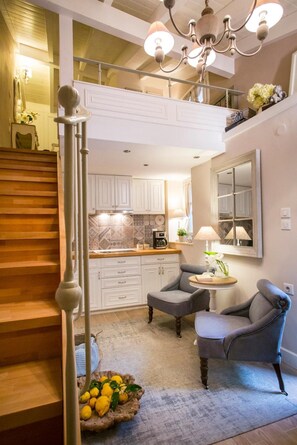 A modern kitchen with white cabinets, a dining area with two grey chairs, a chandelier, and a staircase.