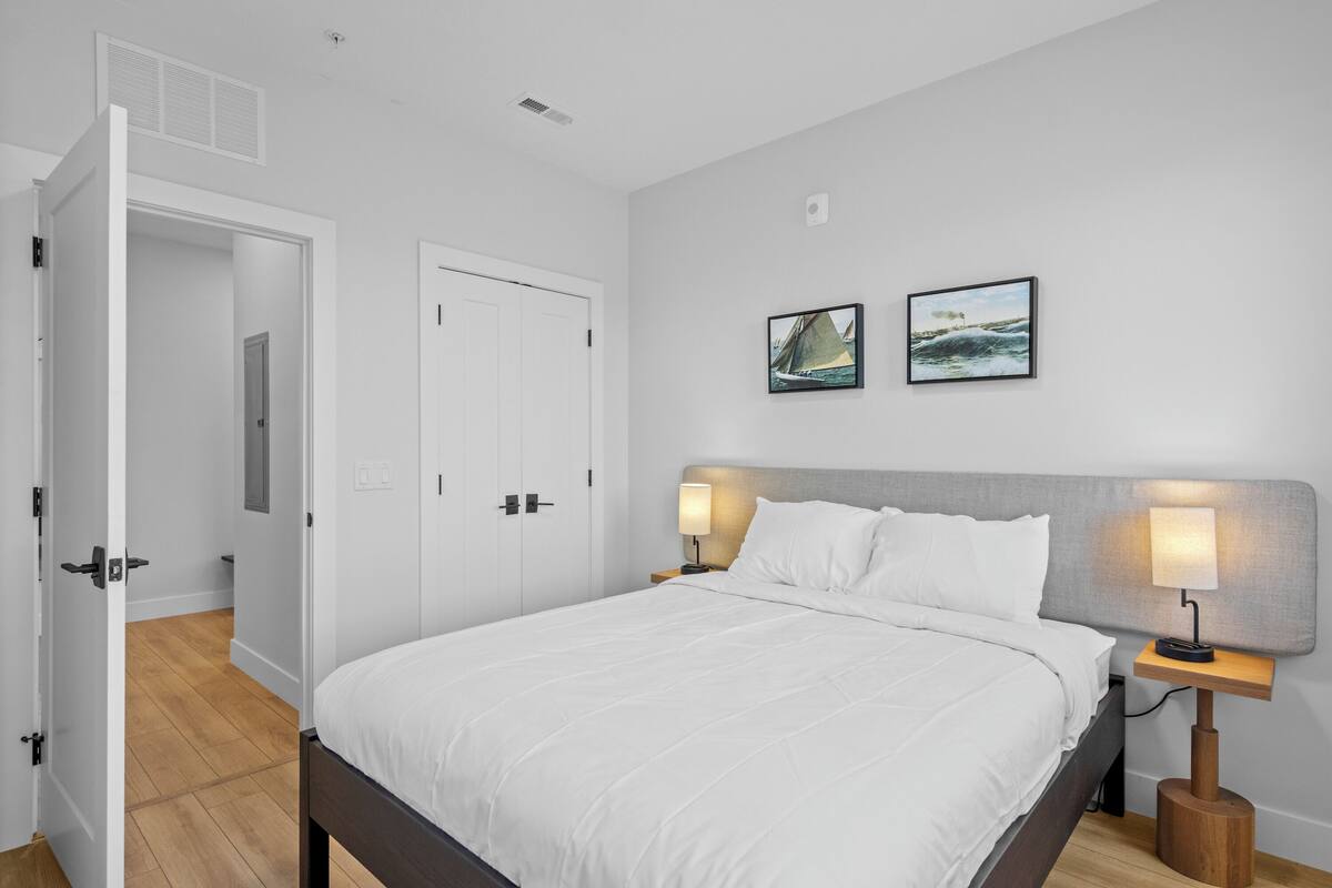 A bedroom with a bed, two bedside lamps, a nightstand, and two framed pictures on the wall.