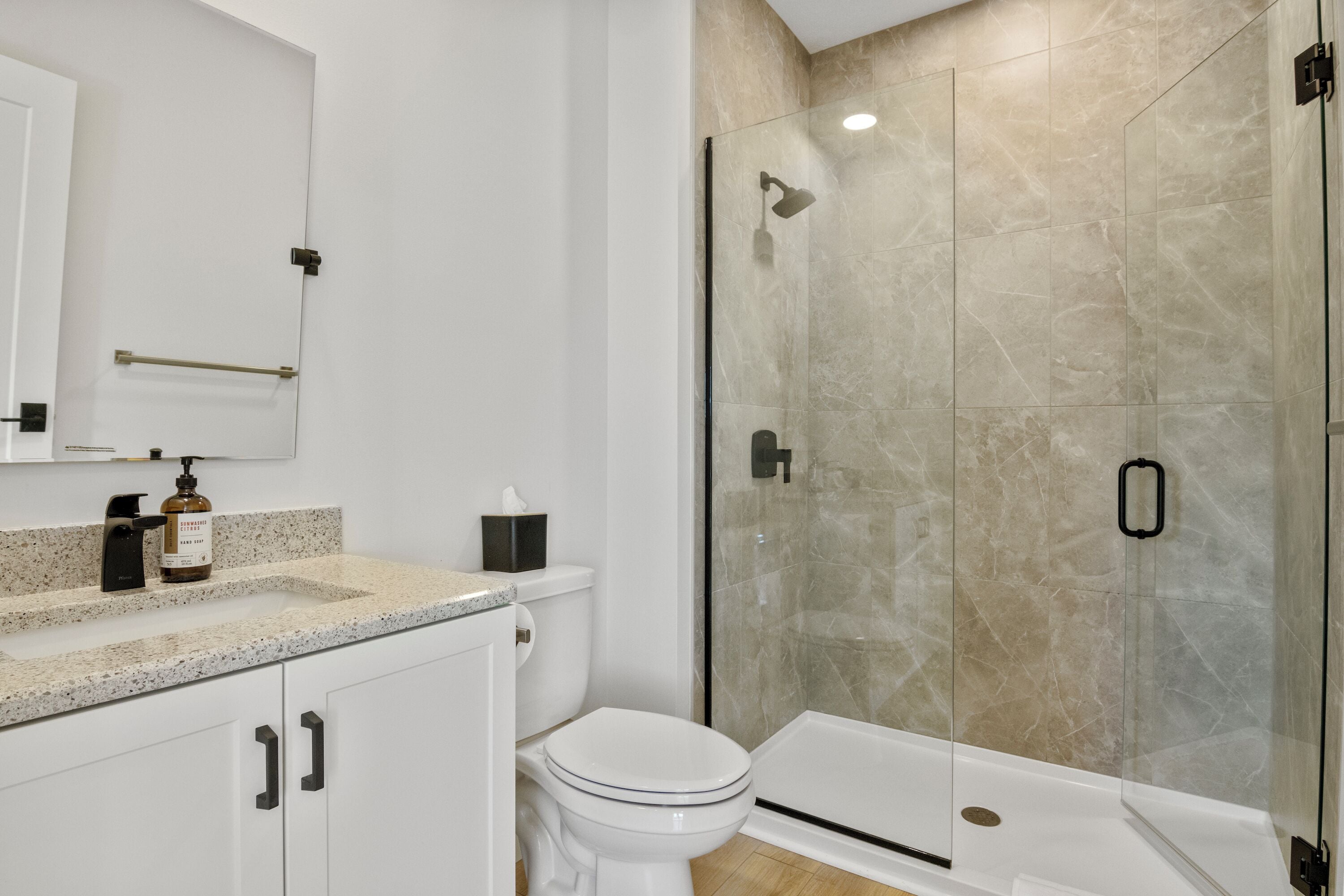 A modern bathroom with a glass-enclosed shower, a toilet, and a sink with a soap dispenser.