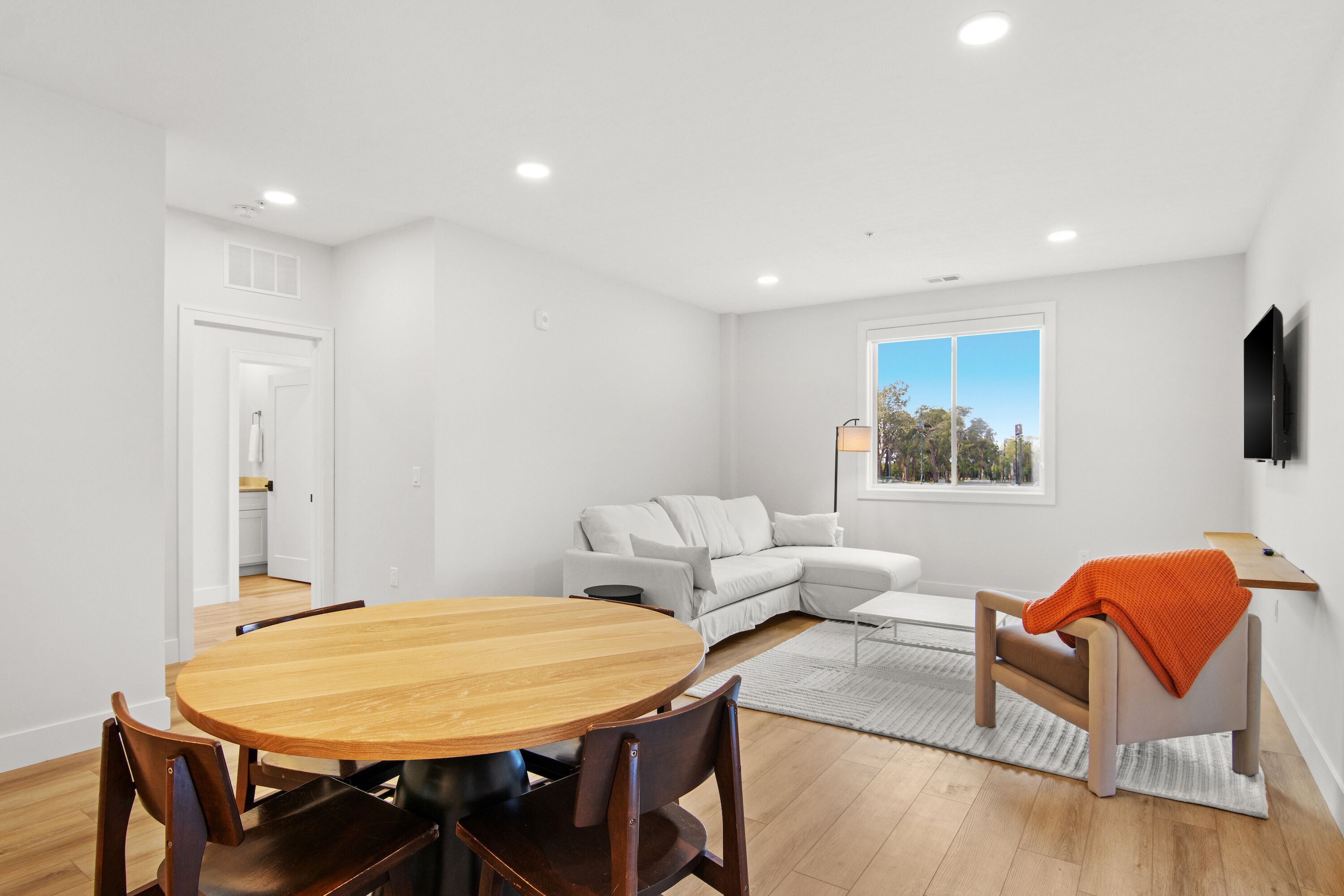 Un salón moderno con una mesa de comedor de madera, sofá blanco y vistas al exterior a través de un ventanal grande.