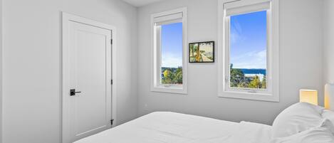Ein Schlafzimmer mit einem großen Bett, zwei Fenstern mit Blick, einer Tür und einem Wandbild.
