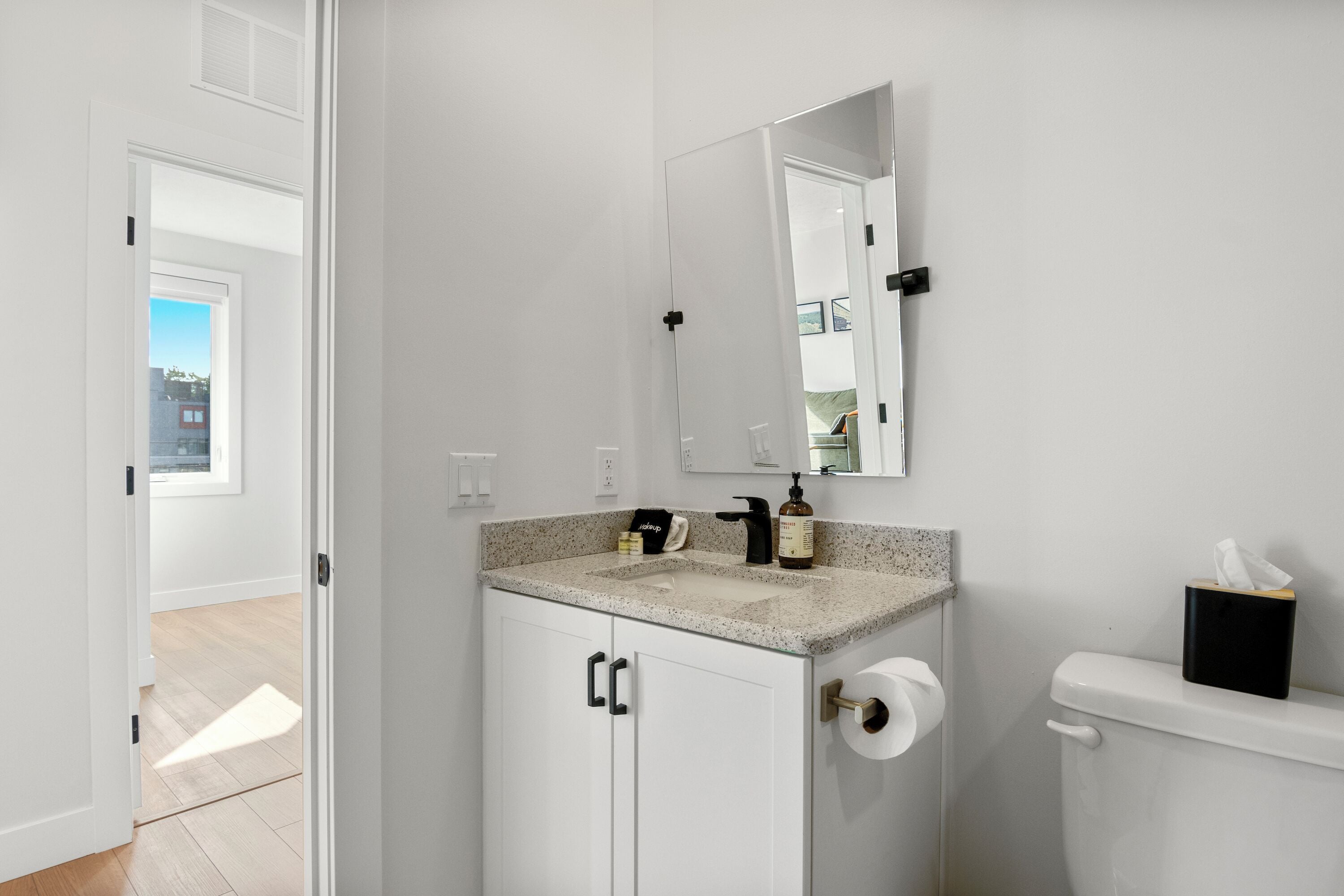 Un baño moderno con tocador blanco, un espejo, inodoro y ventana que deja entrar luz natural.