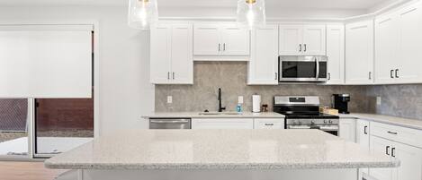 A modern kitchen with white cabinets, a granite countertop, and a central island with wicker chairs.
