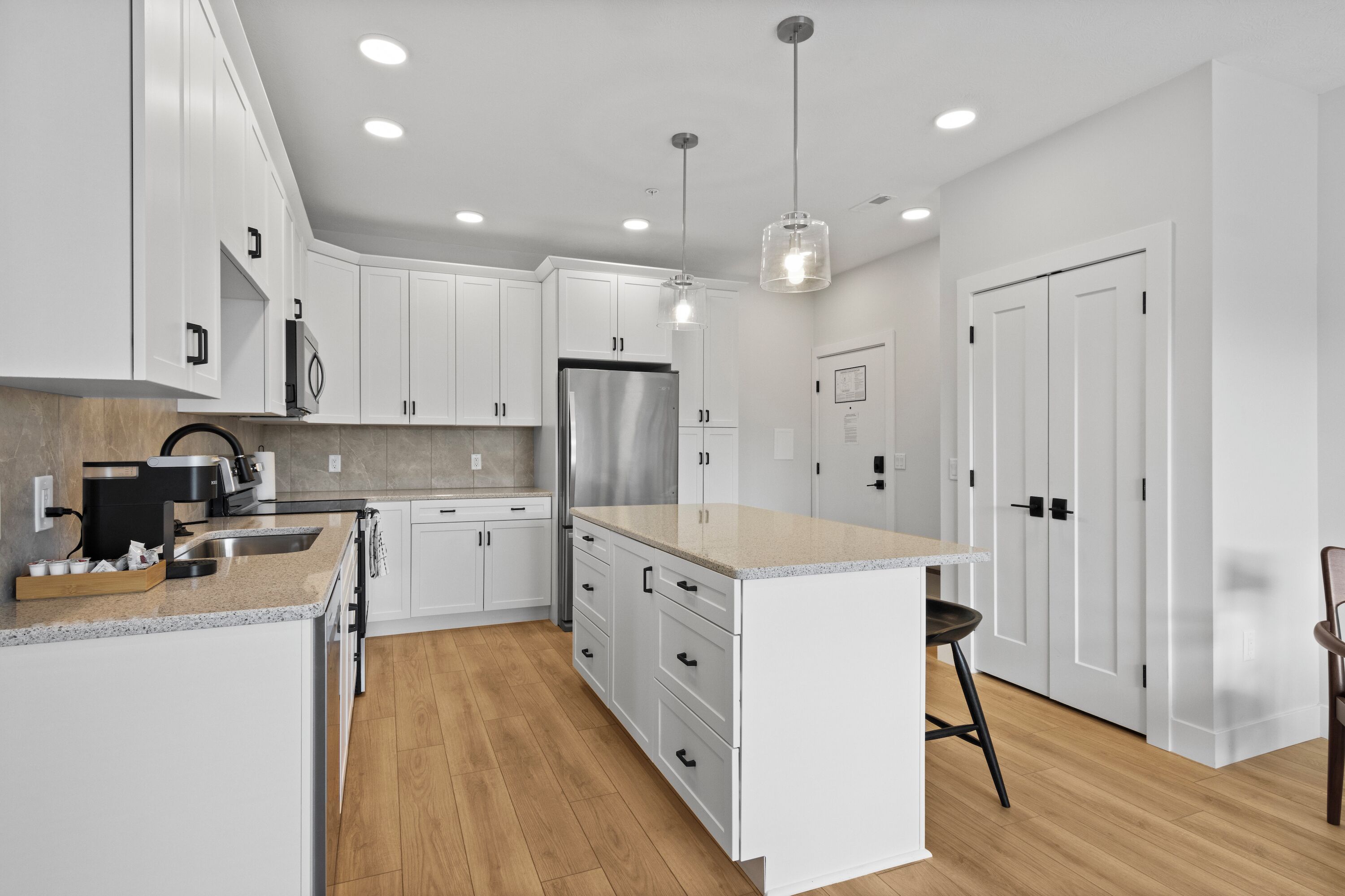 A modern kitchen with white cabinets, a stainless steel refrigerator, and a wooden floor.