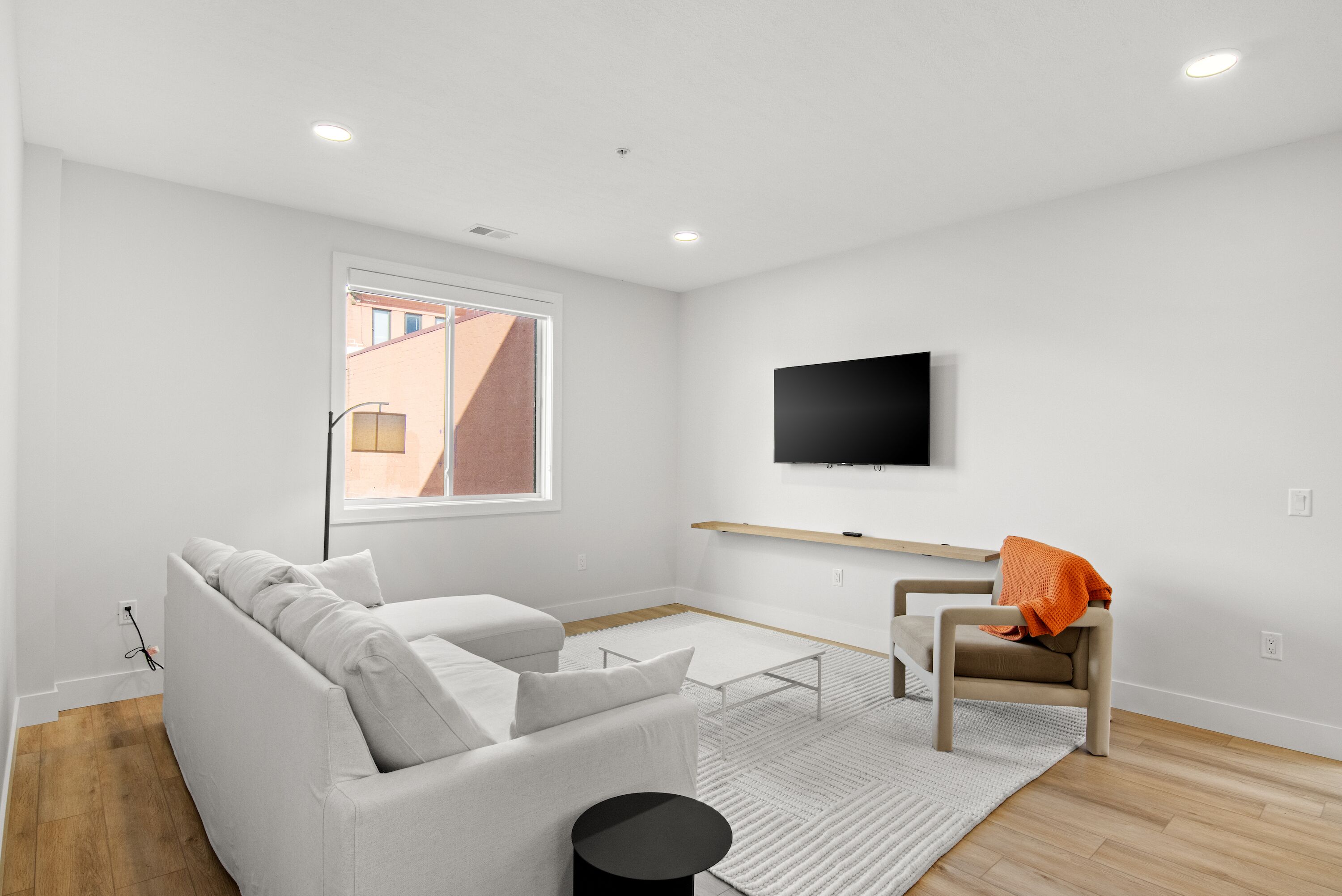 A modern living room with a white sofa, a small table, a chair, and a TV mounted on the wall.