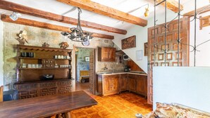 A rustic kitchen with wooden cabinets, a stone wall, and a wooden dining table. - Castle 'Isla Del Burguillo' with Private Terrace, Private Garden and Wi-Fi (Avila)