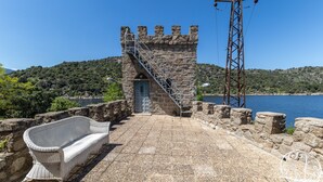A stone building with a staircase leading to a door, a white wicker sofa, and a view of a body of water. - Castle 'Isla Del Burguillo' with Private Terrace, Private Garden and Wi-Fi (Avila)