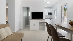 A modern living room with a sofa, a dining table with chairs, a TV on a cabinet, and a kitchen area in the background. - Country House 'Valle Conil' with Private Pool, Wi-Fi and Air Conditioning (Conil de la Frontera)