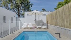 A swimming pool with white lounge chairs and a large umbrella, surrounded by a white fence and a wooden wall. - Country House 'Valle Conil' with Private Pool, Wi-Fi and Air Conditioning (Conil de la Frontera)