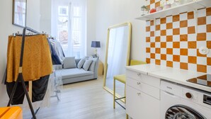 A modern, well-lit room with a sofa, a mirror, a washing machine, and a checkered wall. - Apartment 'Jolie Proche Monaco' with Wi-Fi (Beausoleil)