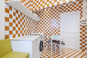 Une cuisine compacte avec un carrelage à motifs, un lave-linge, un évier et un coin repas comprenant une table et des chaises.