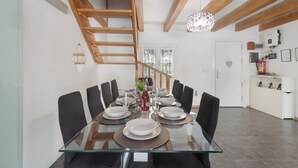 Een eetruimte met een glazen tafel, zwarte stoelen en een houten trap.
