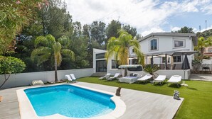 Een zwembad met houten terras, een modern huis met balkon en een verzorgd gazon.