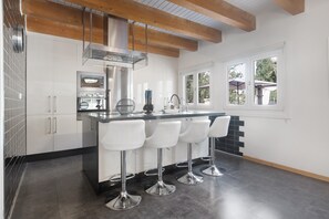 A modern kitchen with white cabinets, a stainless steel range hood, a built-in oven, and a bar area with white stools. - Holiday Home 'Palmera' with Mountain Views, Wi-Fi and Air Conditioning (Pinos de Alhaurín)