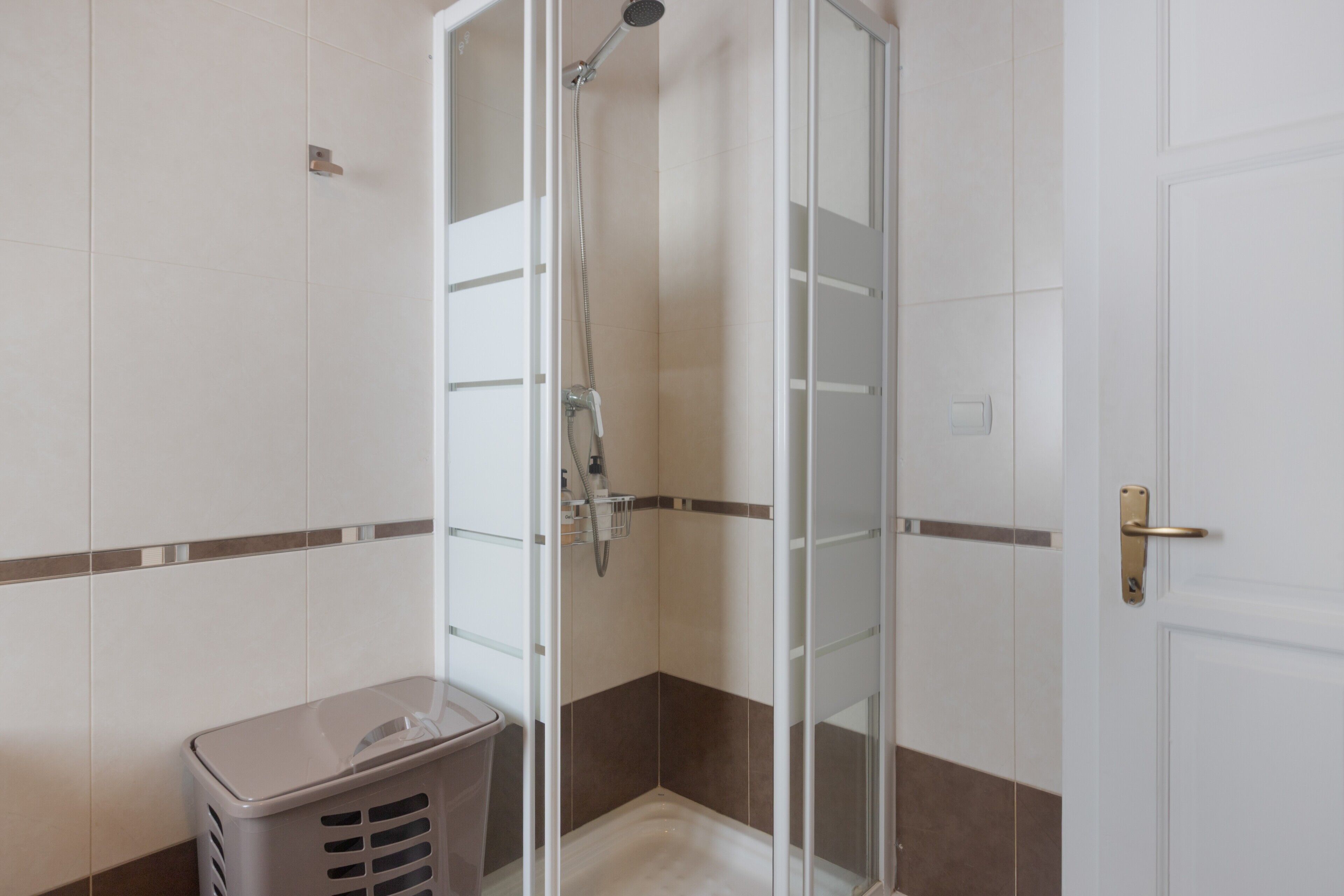 A shower with a glass door, a towel rack, and a laundry basket.