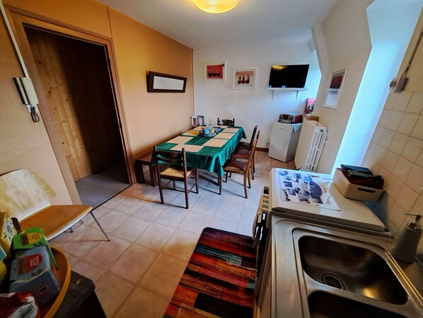 Cocina compacta con lavamanos, una mesa de comedor con sillas, refrigerador y televisor montado en la pared.