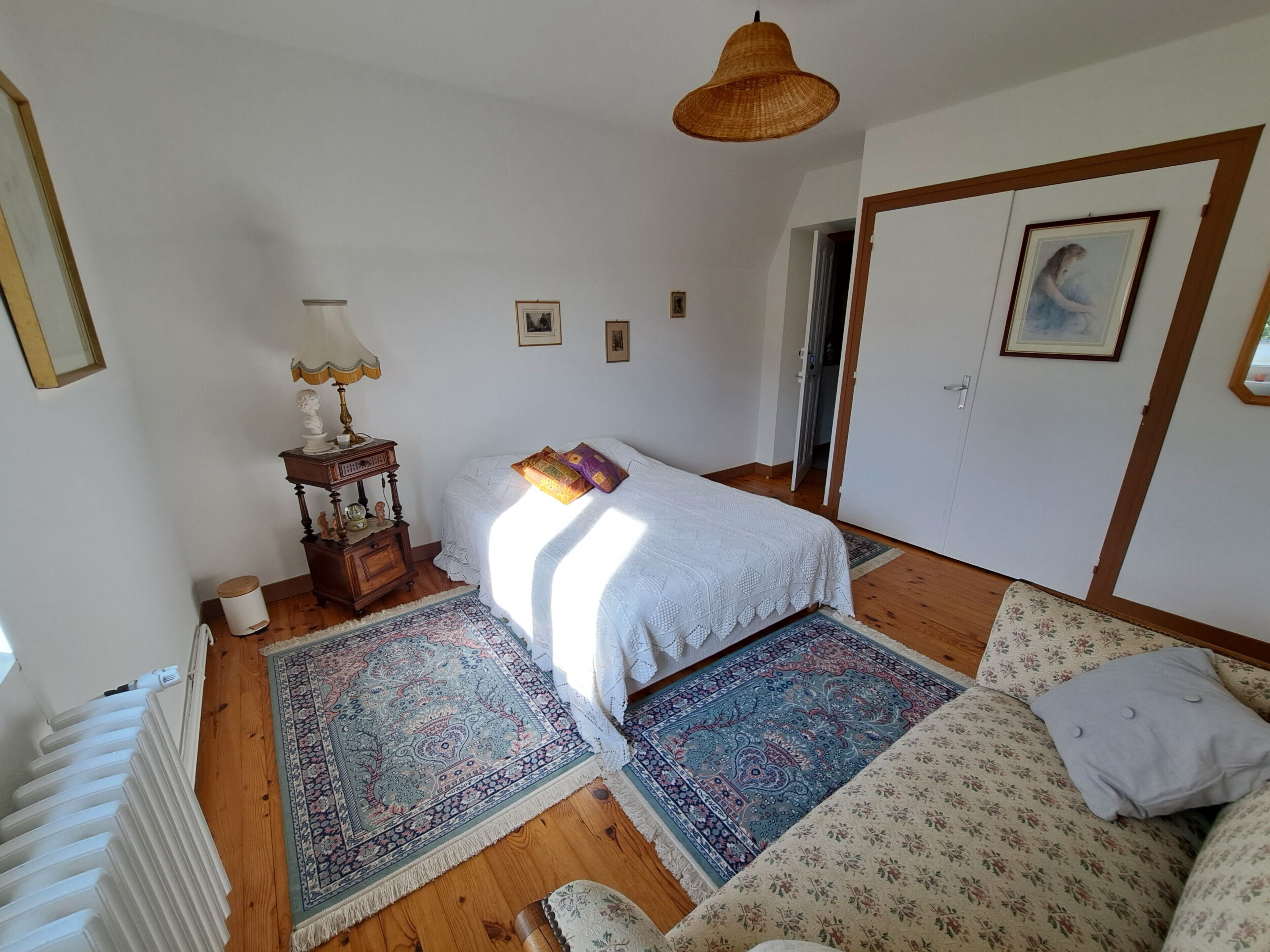 Ein Schlafzimmer mit Bett, Nachttisch, Lampe, Heizkörper, Tür und Fenster.
