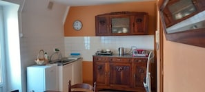 A compact kitchen with a refrigerator, sink, wooden cabinets, a clock, and a radio.