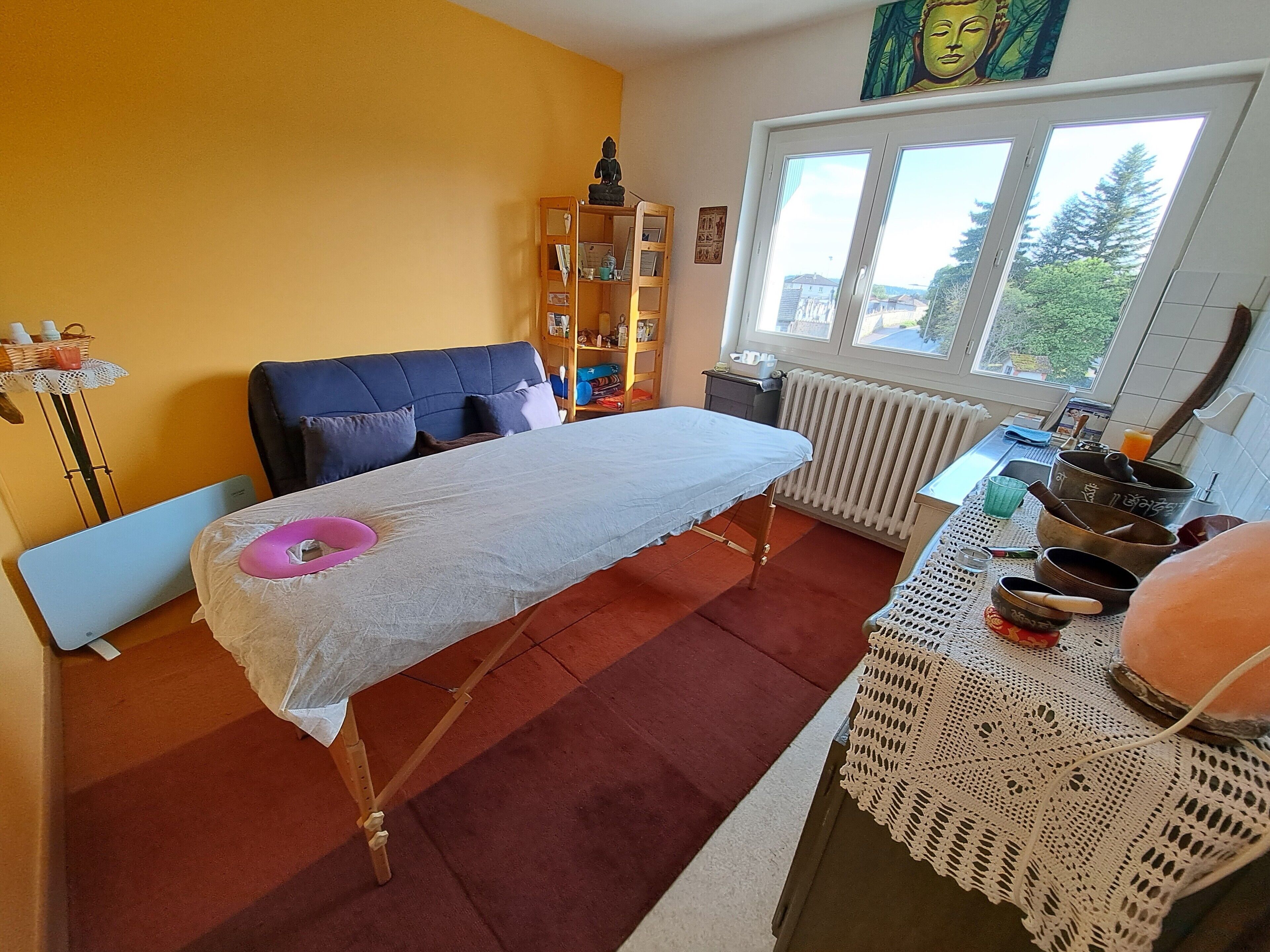 Een kamer met een massagetafel, een raam met uitzicht, een boekenkast en een klein tafeltje met schalen.