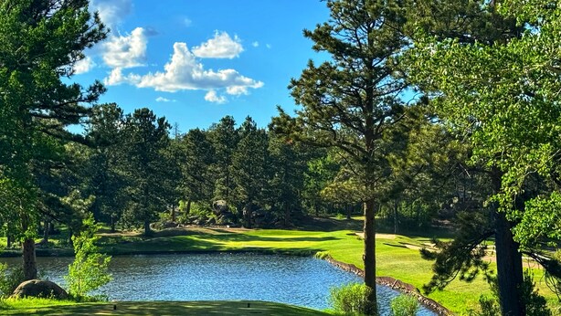 A golf course with a pond, surrounded by trees and a clear sky. - The Golf Club at Fox Acres (Red Feather Lakes)