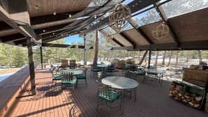 An outdoor patio with wooden flooring, green cushioned chairs, and tables. - The Golf Club at Fox Acres (Red Feather Lakes)