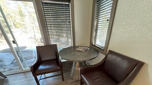 A room with a round table and two leather chairs, large windows with blinds, and a view of the outdoors. - The Golf Club at Fox Acres (Red Feather Lakes)