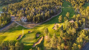 An aerial view of a golf course with a clubhouse, surrounded by dense forests and mountains. - The Golf Club at Fox Acres (Red Feather Lakes)