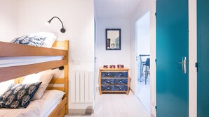 A room with a bunk bed, a small wooden dresser, a mirror, and a teal door.
