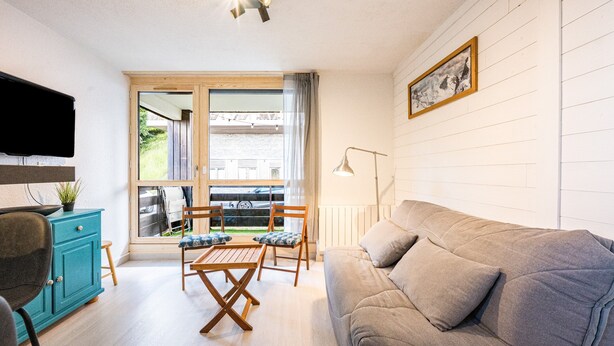 A living room with a sofa, a coffee table, a TV, and a window with a view of the outside.