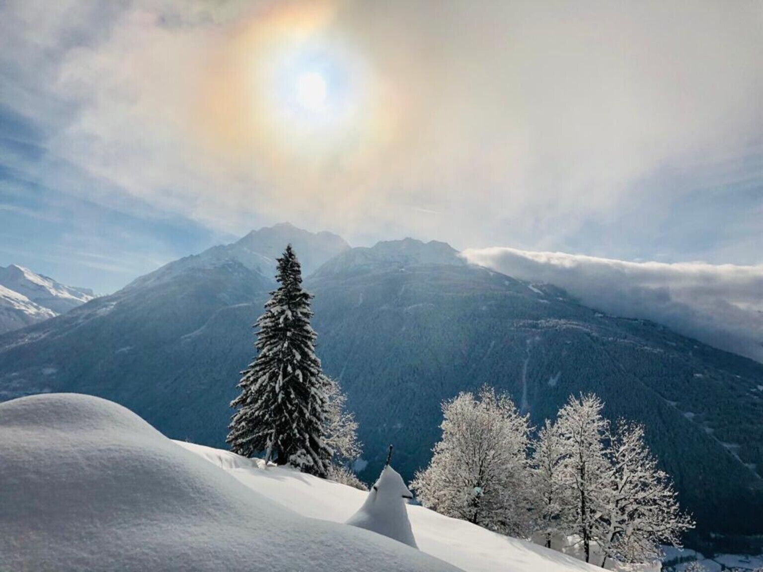 A snowy mountain landscape with a clear sky and a sun halo.