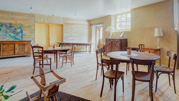 Une pièce spacieuse avec un plancher en bois, une table à manger, des chaises, un buffet et un tableau accroché au mur.