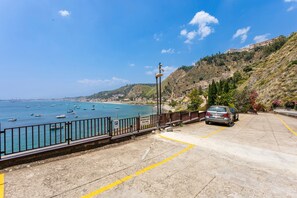 A coastal parking area with a car, a sign indicating a parking area, and a view of the sea with boats. - Apartment 'Giulia's On The Sea' with Shared Pool, Wi-Fi and Air Conditioning (Taormina)